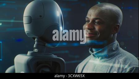 Close Up of Guy Smiling Warmly While Looking Futuristic Robot With AI and Shiny Details. Positive Interaction Between Humans and AI, Trust, Friendly Future of Robotics and Technological Partnership. Stock Photo