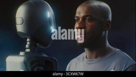 Close Up Man's Face Next Sleek, Dark Robot, Both Gazing With Neutral Expression. Concept of Integration of AI and Robotics Into Industrial or Daily Life, Future of Work and Technological Progress. Stock Photo