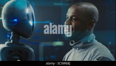 Close Up of Guy Smiling Warmly While Looking Futuristic Robot With AI and Shiny Details. Positive Interaction Between Humans and AI, Trust, Friendly Future of Robotics and Technological Partnership. Stock Photo