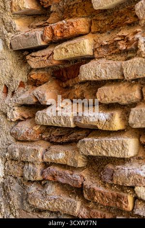 An ancient brick wall with a few bricks eroded and missing. The wall is brown and has a rough texture. The missing bricks create a sense of emptiness Stock Photo