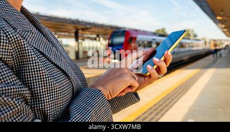 Businesswoman using smartphone in front of passenger train on railway platform Stock Photo
