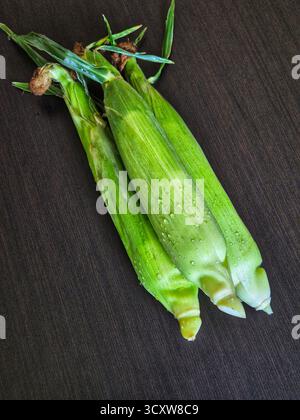 Three fresh corn cobs in their green husks on wooden background. corn on the cob Stock Photo