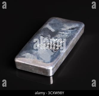 Cast silver bar, side view on black glass plate and background. Silver ingot with an irregular surface created by the cooling of the liquid metal. Stock Photo