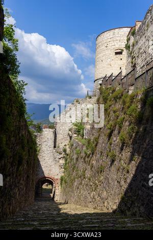 View of Torre Coltrina rising above stone passage Strada del Soccorso inside Brescia Castle, framed by massive limestone walls and blue sky Stock Photo