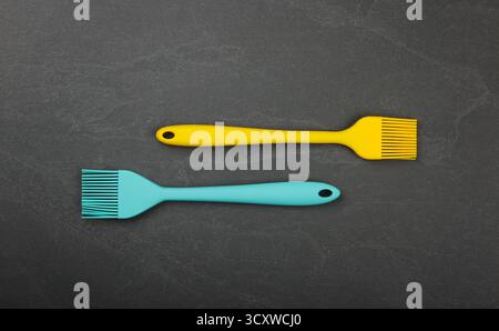 Two silicone brushes for pastry or basting on black slate board with copy space, colorful modern culinary kitchen utensils, close up, elevated table t Stock Photo