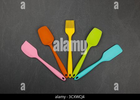 Five silicone cooking spatulas and brushes on black slate board with copy space, colorful modern culinary kitchen utensils, close up, elevated table t Stock Photo