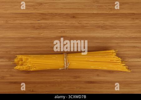 Bundle of uncooked dry spaghetti tied with string, resting on a wooden cutting board, ready for cooking and italian cuisine preparation, top down view Stock Photo