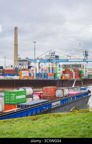 Cargo boat maneuvering in the docks with stacks of shipping containers in the background Stock Photo
