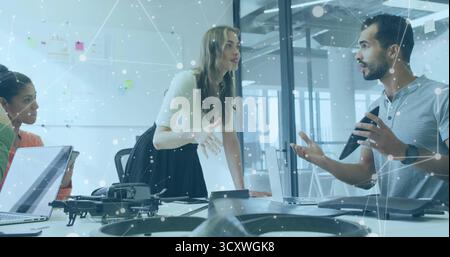 Discussing drone project, three colleagues leaning around conference room table with quadcopter Stock Photo