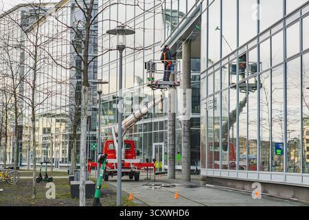 A worker in safety gear on a lift cleaning large glass windows of a modern building Stock Photo