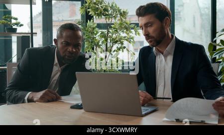 Diverse business team two businessmen Caucasian African American men with laptop documents review in office working colleagues discuss data analyzing Stock Photo