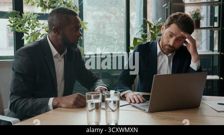 Two diverse business men team upset with bad result businessmen workers multiracial partners in office difficulty trouble with papers and laptop Stock Photo