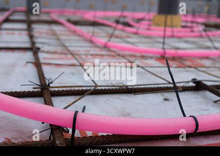 Pink pipes are arranged on a metal rebar grid and secured with black zip ties on a construction site, before concrete is poured for in-floor radiant heating system. Stock Photo