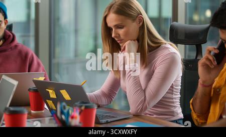 Three concentrated business professional multiracial colleagues at table informal working company busy job task Caucasian woman with laptop Indian men Stock Photo