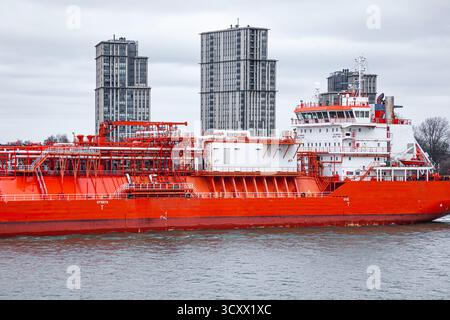 A gas carrier goes along the canal, accompanied by a tug in the city of Rotterdam, the Netherlands Stock Photo