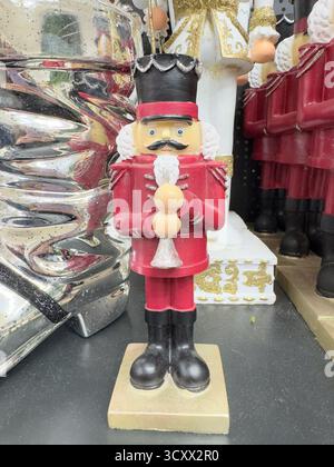 Festive nutcracker in regal red uniform stands proudly with silver-crowned hat and white beard, clutching ornaments. Stock Photo