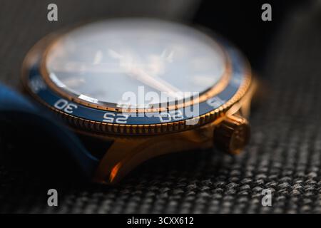 A close-up photograph of a bronze  wristwatch resting on a textured fabric surface. The blue bezel and polished crown highlight craftsmanship, luxury, Stock Photo