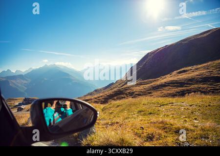 Travel by car. Driving a vehicle on a mountain road. View of a high mountain landscape on a sunny day. A woman sits in a car and takes a photo. Grossg Stock Photo