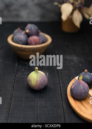 Close up of ripe figs on a brown wooden plate and bowl against a dark background, styled with rustic tones and soft depth Stock Photo