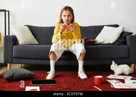 A girl relaxes on the couch, gaming with her controller in a cozy home atmosphere. Stock Photo