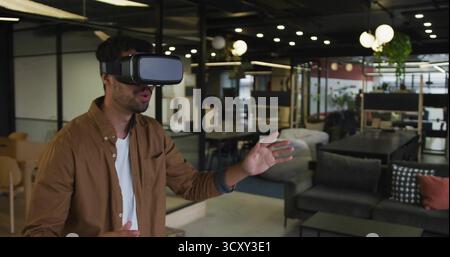 Interacting man wearing VR headset gesturing in coworking lounge, with desks, copy space Stock Photo