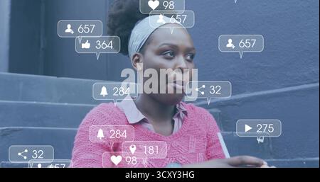 Gazing woman in pink sweater headband sitting on steps by grey wall with phone notification icons Stock Photo