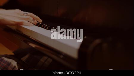 Pressing pianist's hands wearing silver rings playing piano keys in studio, plaid skirt, copy space Stock Photo