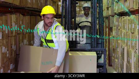 Lifting cardboard box, worker wearing neon vest in warehouse aisle, with moving forklift behind Stock Photo