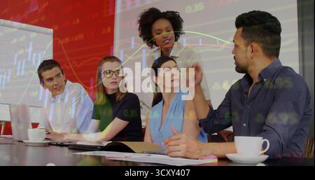 Professionals discussing financial graphs sitting around table in conference room, with notebooks Stock Photo