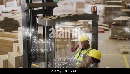 Two workers wearing safety vests inspecting pallet stacks by forklift in warehouse, with clipboard Stock Photo