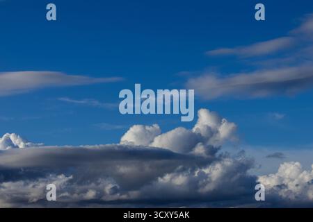 Fluffy and dramatic clouds fill a vibrant blue sky, with darker, more ominous clouds gathering below a brighter, cumulus formation. Stock Photo