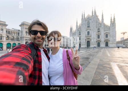 Happy couple taking selfie in front of Duomo cathedral in Milan, Lombardia - Two tourists having fun on summer vacation in Italy Stock Photo