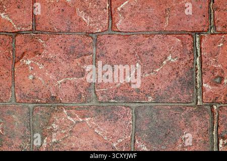 Close-up of an aged red brick pavement showing detailed texture, cracks, and weathering, forming a rustic surface pattern ideal for backgrounds, archi Stock Photo