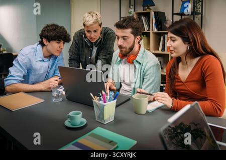 A dedicated team of four young multi-ethnic students and colleagues collaborating on a project, gathered around a laptop with focus and concentration Stock Photo