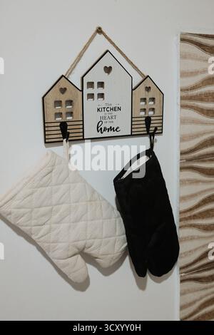 Decorative kitchen wall hanger shaped like houses with oven mitts. Cozy rustic detail ideal for home decor, cooking, or lifestyle projects. Stock Photo