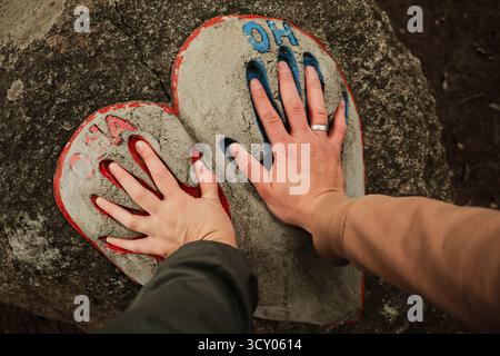 Close-up of man and woman placing hands over red and blue handprints on a heart shaped stone. Perfect for love, unity, and relationship themes. Stock Photo