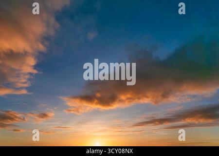 Colorful dramatic sunset sky with orange, blue and gray clouds. Golden hour twilight cloudscape background with vibrant warm colors fading into evenin Stock Photo