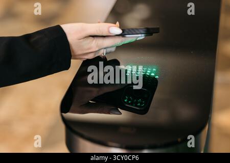 Woman's hand interacts with smartphone above a glossy black surface, illuminated by green light, highlighting technology and user engagement in a mode Stock Photo