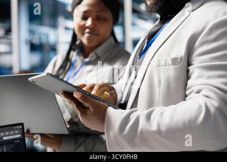 Close up of developers in data center using tablet to update infrastructure software, configuring network virtualization. Server hub IT professionals using device to verify hardware settings Stock Photo