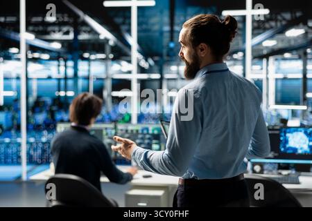 Teamworking admins coding in data center, updating AI driven automation scripts. Server room colleagues programming artificial intelligence algorithms, debugging infrastructure Stock Photo