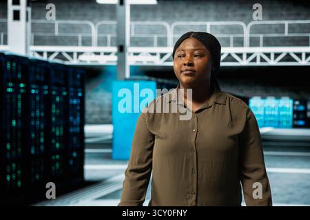 System administrator walking through server farm rows lined with storage infrastructure rigs. IT specialist inspecting high tech data center helping power online services for enterprise customers Stock Photo
