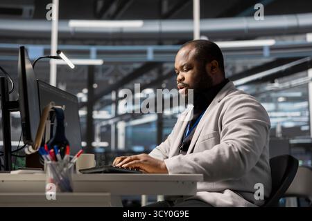 Data center system administrator running diagnostic scripts, examining infrastructure. Man working in server hub using PC to evaluate performance metrics, running tests to maintain system stability Stock Photo