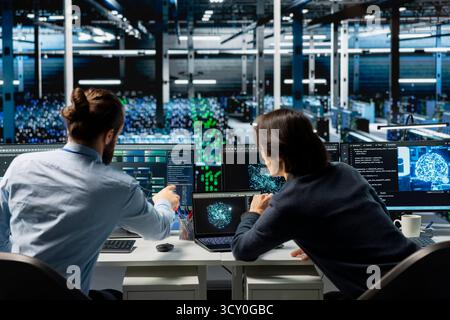 System administrators coding in data center, updating AI driven automation scripts. IT experts working in server room, programming artificial intelligence algorithms, debugging equipment Stock Photo