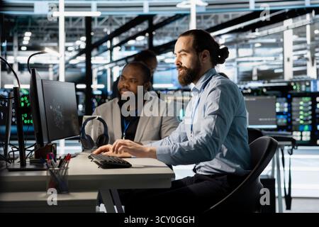 Team of programmers using computer in server farm, analyzing data. Men working in data center office examining infrastructure using device, ensuring system integrity and security Stock Photo