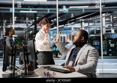 Delighted data center colleagues doing high five, celebrating successful AI implementation. Happy server hub engineering team excited after optimal results achieved by artificial intelligence model Stock Photo