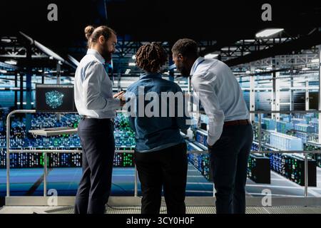 Data center system administrators using laptop to review AI LLM visualization. African american team of engineers use devices to analyze neural network outputs, ensuring stable operations. Stock Photo