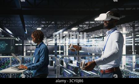 Data center programmers on industrial platform using virtual reality tech, collaborating on tasks. Server room IT professionals visualizing large language model architecture using VR headset Stock Photo