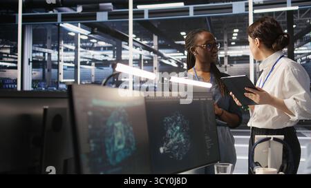 Software developers working together in server farm, reviewing neural network code and LLM visualization dashboards. Teamworking data center colleagues monitoring AI system performance, camera A Stock Photo