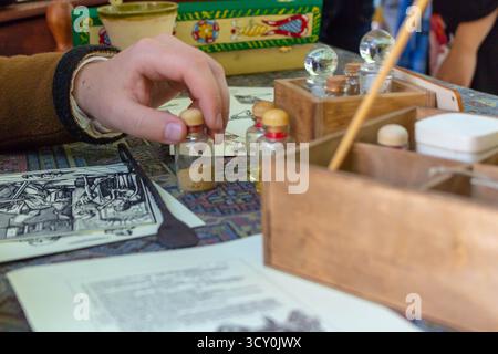 A medieval apothecary carefully holds small glass bottles with powders and liquids on a wooden table during historical reenactment Stock Photo