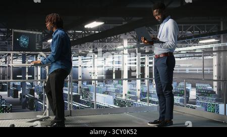 System administrators in data center using laptop to monitor neural network LLM visualization. Server hub teamworking colleagues overseeing rigs powering machine learning processes, Stock Photo